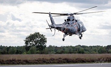 Colorful military helicopter hovering above the open field during daytime, showcasing aviation technology and aerial maneuvering skills.