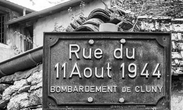 Street sign marking Rue du 11 Août 1944 in black and white, highlighting historic significance of WWII bombing in Cluny. Rustic black and white photograph of a historical street sign on Rue du 11 Août 1944, commemorating the WWII bombing of Cluny, France with aged textures and vintage urban elements.