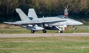 FA18 fighter jet taxiing on runway during day, sophisticated aircraft with twin tail fins and weapons payload, pilot in cockpit preparing for takeoff.