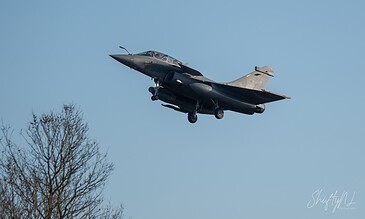 Fighter jet in mid-air during flight, showcasing sleek design and dynamic movement against a clear blue sky.
