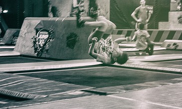 1. Young person falling during a trampoline park indoor activity, captured in black and white, showcasing action and energy in a dynamic sports environment.