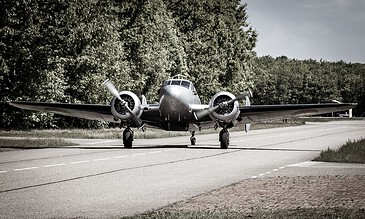 An iconic vintage airplane parked on a rural airstrip, surrounded by lush greenery and clear skies, capturing a timeless moment of aviation history.