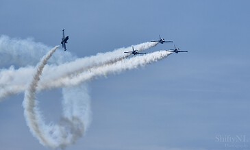 2. Stunning aerial display captured during an airshow, featuring four planes in flight with dramatic smoke trails in the sky. 1. Four sleek aerobatic planes performing a synchronized stunt with white smoke trails against a clear blue sky.