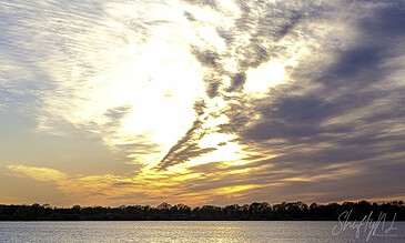 A stunning sunset over a calm lake with dramatic cloud formations and vibrant colors, captured in nature photography style.