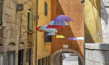 Colorful umbrellas hanging in an alleyway against yellow and orange historic buildings, creating a whimsical and charming atmosphere.