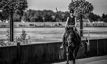 A female police officer riding a horse along a pathway, capturing a moment of equestrian police work outdoors in black and white.