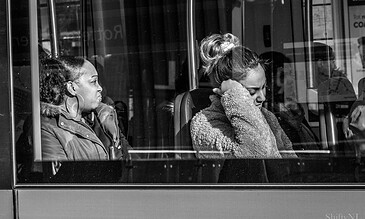 1. Black and white photo of two women on a bus, one looking out the window with a calm expression and the other talking on the phone, capturing everyday life moments.