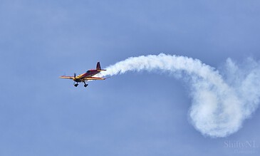 Capturing breathtaking moments of aerial acrobatics and aviation skills in one stunning shot. Vibrant yellow and red aerobatic plane performing a mid-air stunt with a white smoke trail against a clear blue sky.