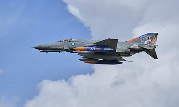 1. A military fighter jet flying through a blue sky with clouds during an airshow, showcasing aerial precision and power.