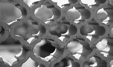 Close-up of concrete lattice wall emphasizing geometric shapes and textures in black and white, highlighting architectural artistry. Intricate concrete lattice wall with geometric patterns in black and white, showcasing architectural detail and craftsmanship.