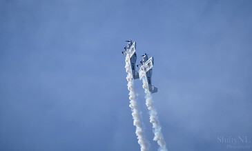 Dynamic airshow performance capturing precision flying and smoke effects by aerobatic planes. High-speed aerobatic aircraft performing a synchronized stunt with vapor trails against a clear blue sky.