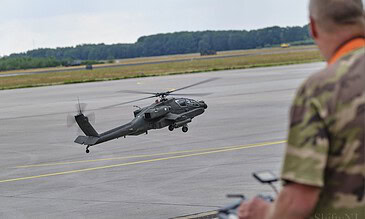 1. Scale model Military helicopter taking off from an airfield under cloudy skies with a pilot in camouflage in the foreground.