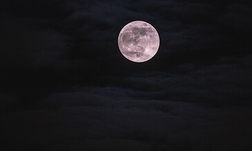 A bright full moon shining through dark clouds against a night sky.