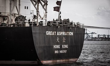 GREAT ASPIRATION cargo ship in Hong Kong harbor with cranes and port infrastructure in the background. A large cargo ship named "GREAT ASPIRATION" sailing in the harbor with industrial cranes and dockyards in the background.