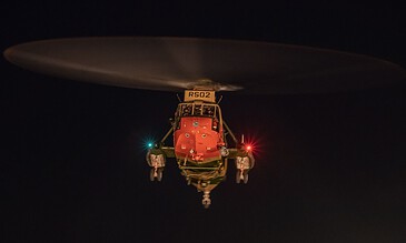 High-resolution night photo of a helicopter in flight with illuminated navigation lights against a dark sky.