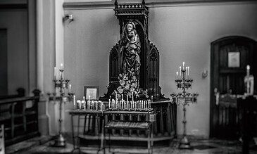 1. Vintage black and white photograph of a religious altar with candles and a Madonna statue inside a church.