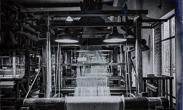 A detailed black and white photo of an old wooden loom in a cozy workshop, showcasing the art of traditional weaving with natural light highlighting the machinery. A vintage textile loom in a rustic workshop with natural light coming through large windows, capturing the intricate process of weaving fabrics; black and white photo emphasizing craftsmanship.