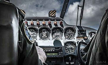 1. cockpit of a vintage aircraft with analog gauges and controls under a cloudy sky.