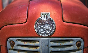 An up-close shot of a vintage red tractor's front, highlighting the rusted metal surface and classic emblem, evoking a sense of agricultural history and nostalgia. Close-up of an old, rusty red tractor hood with a vintage emblem, showcasing weathered metal and nostalgic agricultural machinery details.