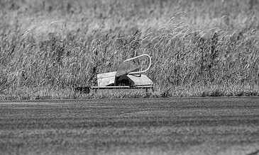A vintage wooden boat resting among tall grasses in a peaceful, overgrown field, captured in black and white for a timeless, artistic effect. A lush, overgrown field with a vintage wooden boat partially hidden among tall grasses, creating a serene and nostalgic scene.
