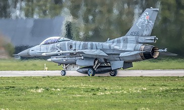 1. Modern fighter jet in camouflage livery taxiing on runway with a blur background of trees and water reflections.
