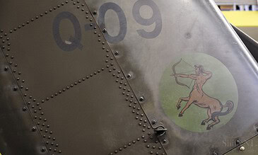 An Apache's metallic body featuring rivets, the registration number Q-09, and a classic heraldic lion emblem with a bow and arrow. Perfect for aviation photography enthusiasts.