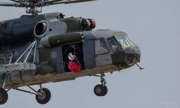 Helicopter in flight with crew member preparing for rescue mission, detailed aircraft captured against a cloudy sky.