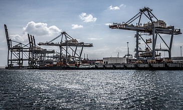 2. A busy port featuring towering cargo cranes and container ships, showcasing maritime shipping and industrial infrastructure near the waterfront. 1. Industrial port with large cargo cranes and ships under a partly cloudy sky, capturing maritime logistics and shipping activities.