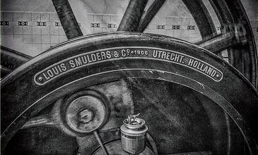 A black and white photo of an old factory machine with detailed engravings, highlighting historical industrial artistry and vintage machinery. Louis Smulders & Co. Utrecht Holland vintage industrial machinery, black and white photo, historic engineering, mechanical details, classic Dutch manufacturing industry.