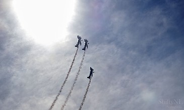 Spectacular airshow with fighter jets flying in formation and leaving smoke trails against a clear blue sky, showcasing aviation skill and precision. Bright blue sky with three fighter jets performing an aerial stunt, leaving smoke trails behind, captured under sunlight for dramatic effect.