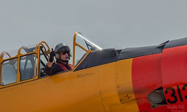 High-angle shot of a pilot in cockpit of a vintage yellow and orange fighter jet, preparing for takeoff against a cloudy sky.
