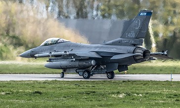 F-16 fighter jet taxiing on runway with blurred background of trees and sky, showcasing military aircraft in action.