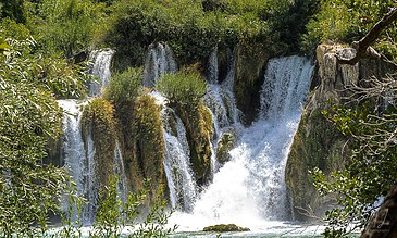 A waterfall cascading over rocks surrounded by lush green foliage in a natural setting.