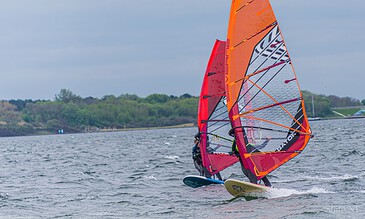 Vivid windsurfing sails showcasing action and thrill on the water, perfect for outdoor sports and water sport photography. Colorful windsurfing sails on the water, capturing exciting moments of windsurfing adventure at a scenic lakeside location.