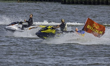 Jet skis racing on the water with a bold flag in the background, capturing dynamic moments of fun and adrenaline on a sunny day.