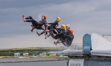 2. Exciting water sport activity captured with friends in wetsuits and helmets jumping into water, showcasing teamwork and fun at the waterfront. 1. Group of people in wetsuits and colorful helmets jumping off a platform into water during water sport activity.