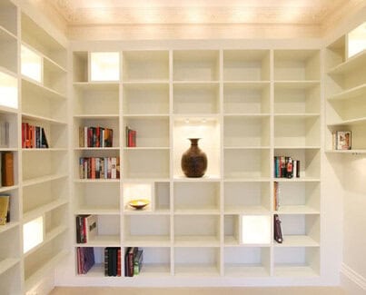 Tall White painted bookcases on 3 walls with LED light accent square shelves