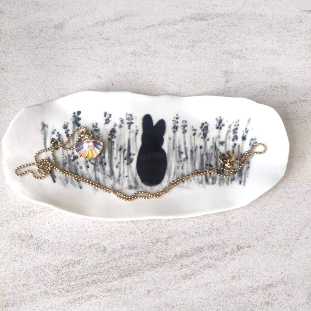A small gold necklace with a colorful pendant rests on the Bunny Jewellery Holder, which features a black silhouette of a rabbit surrounded by floral patterns.