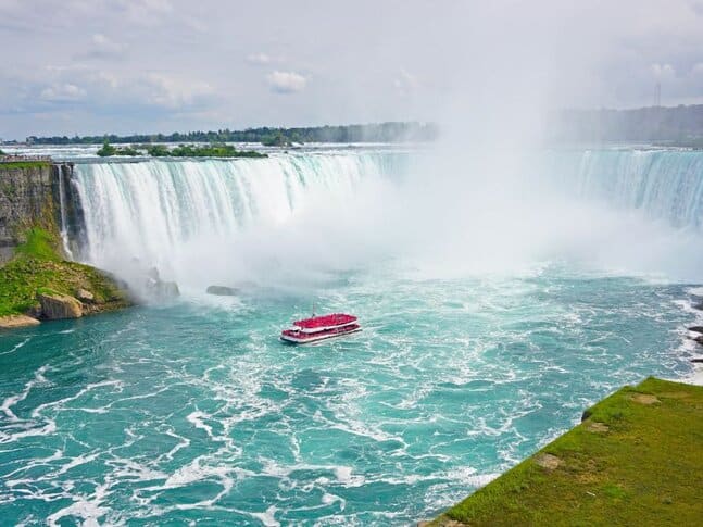 A red boat sailing right up to the mist at the bottom of Niagara Falls