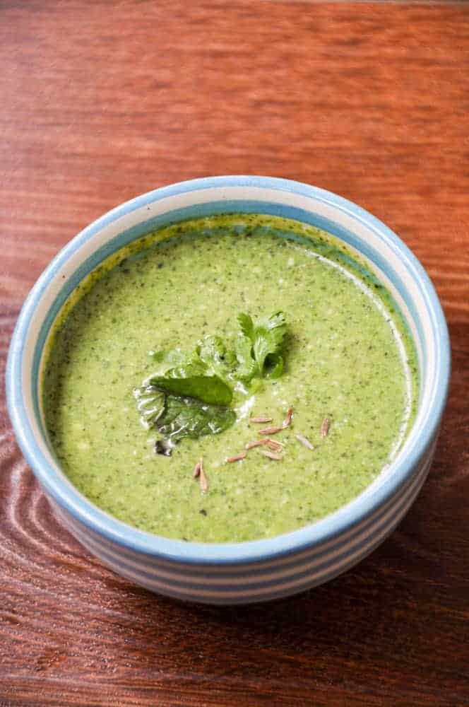 Green Chutney served in small chutney bowl with mont leaves and cumin garnish.