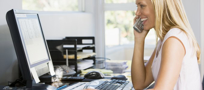 Woman in office with computer using VoIP telephone