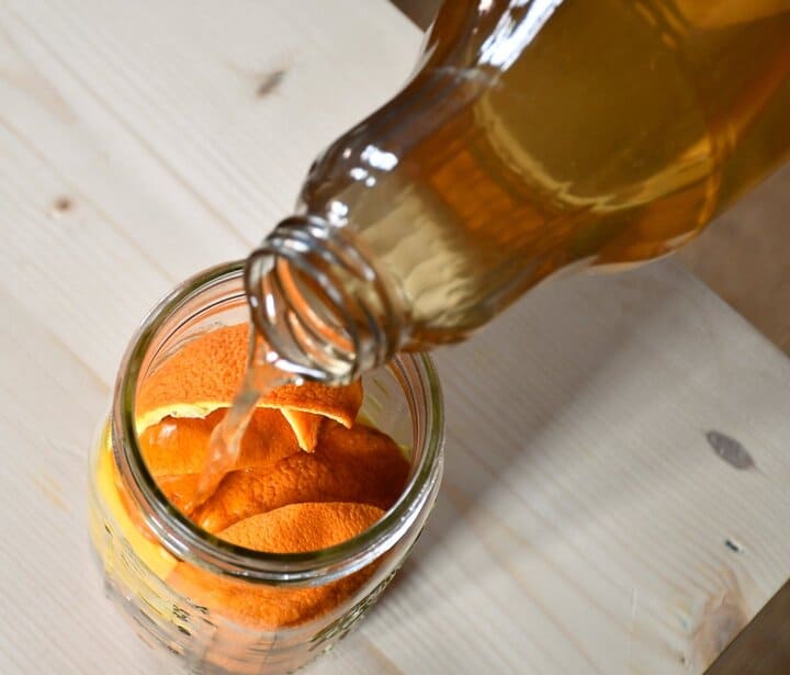 Overhead view of apple scrap vinegar being poured into the jar filled with orange scraps.