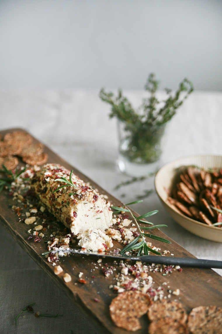 roll of vegan homemade cheese with a nut crust next to some crackers on a wooden surface