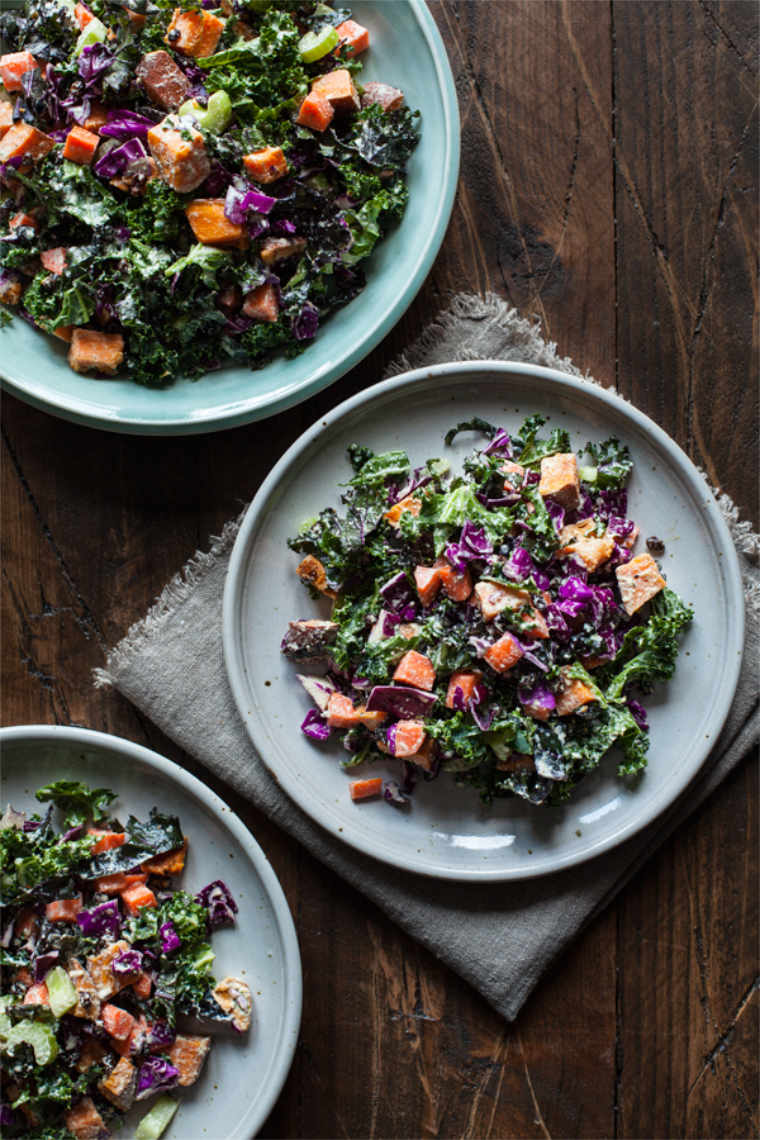 three plates with winter salad consisting of sweet potato, red cabbage, kale and a creamy vegan dressing