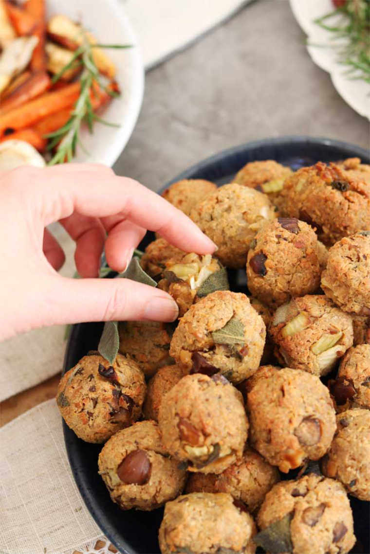 black bowl with a large amount of vegan tempeh stuffing balls and a hand reaching for one of them