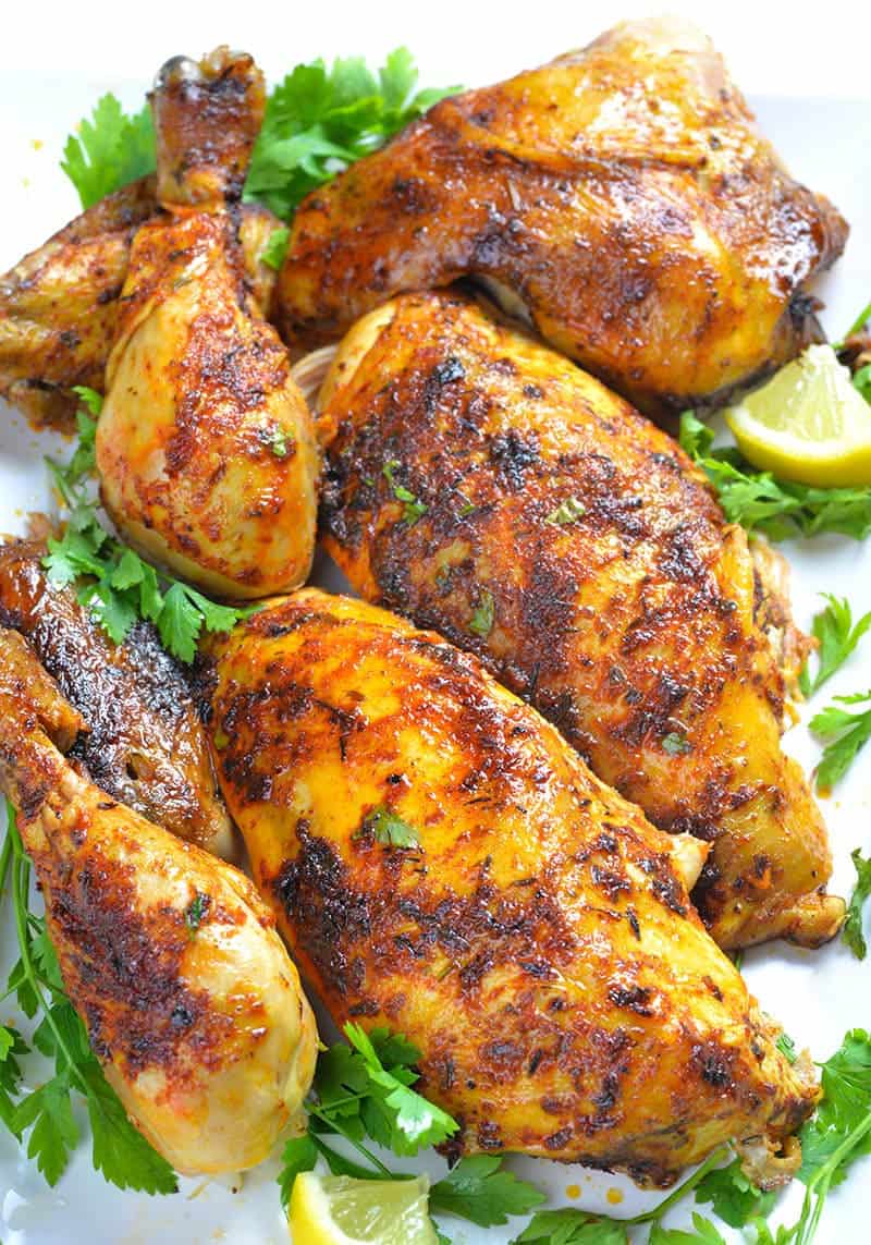 Part of Whole chicken cooked in a slow cooker laying on big white plate and garnished with parsley.