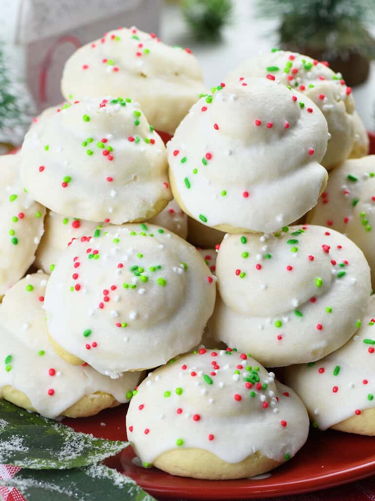 A plate piled with Italian Christmas cookies, each topped with a white icing and decorated with red, green, and white sprinkles, giving them a festive holiday look.