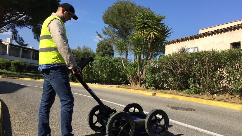 a person uses a GPR on a paved road in a suburb