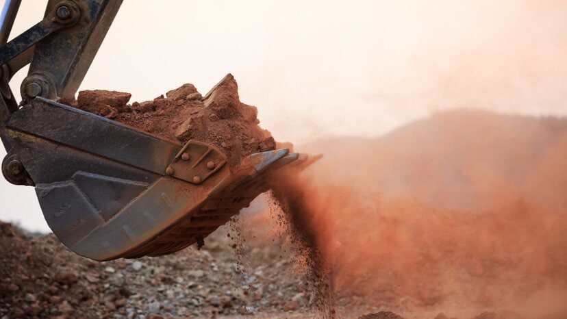 an excavator working with dusty red soil
