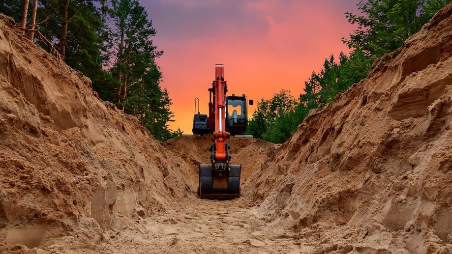 an excavator digs into a ground against a forest background